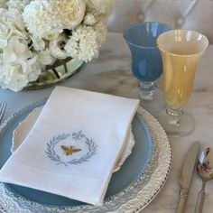 a place setting with white flowers and blue glassware on a marble dining table top