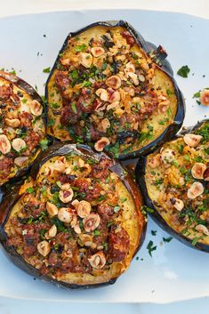 four stuffed acorns on a white plate topped with nuts and herbs, garnished with parsley