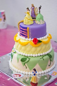 a three tiered cake with princess figurines sitting on it's sides