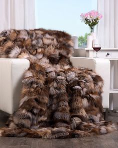 a fur throw sitting on top of a white chair next to a vase with flowers