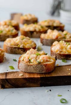 small pieces of bread topped with shrimp on top of a wooden cutting board