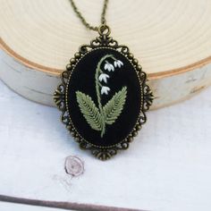 a black necklace with green and white flowers on it sitting on a piece of wood