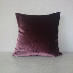 a purple velvet pillow sitting on top of a white table next to a gray wall