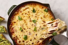 a skillet filled with cheese and spinach on top of a white counter next to slices of bread