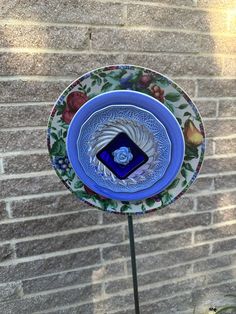 a blue and white plate sitting on top of a metal pole next to a brick wall