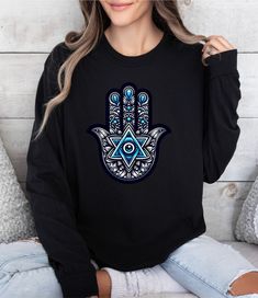 a woman wearing a black sweatshirt with an ornate hamsa hand on it's chest