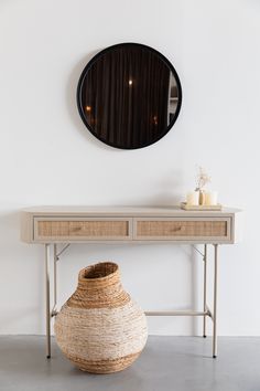 a table with a vase and mirror on it next to a wall mounted round mirror