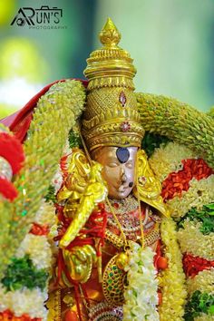 the statue is dressed in gold and surrounded by white flowers, garlands and other decorations