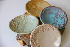 four ceramic bowls sitting on top of a piece of driftwood with lacework designs