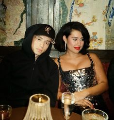 a man and woman sitting at a table with drinks in front of them, posing for the camera