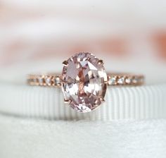 an oval shaped pink diamond sits on top of a white ring with diamonds around it