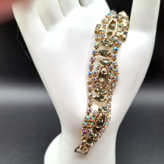 *Description: This is a beautiful mid-century uniquely designed rhinestone bracelet from the late 1950s.  The rhinestones are prong set on a gold tone finish.  The green is more of a moss green rhinestone, marquise cut rhinestones.  The aurora borealis rhinestones are chaton cut round.  The clasp is a fold over hinged clasp. This would be a great addition to your vintage jewelry collection or make a great vintage gift! *Approximate Measurements: Length - 7 1/4 Inches, Width - 7/8 Inch *Condition: Very good vintage condition.  Will see signs of wear under magnification. See photos for details. *Hallmark:  Unsigned *Item # 5961 Please look at the photos carefully as they are a part of the description. We are more than happy to answer any questions you may have prior to purchase. You are look Costume Jewelry Crystal Bracelet With Rhinestones For Party, Crystal Rhinestone Bracelet For Party, Costume Crystal Bracelet With Rhinestones For Party, Vintage Rhinestone Crystal Bracelet For Party, Costume Jewelry Bracelets With Stones For Party, Party Costume Jewelry Bracelets With Stones, Vintage Metal Crystal Bracelet For Party, Sparkling Crystal Bracelet In Costume Jewelry Style, Formal Costume Jeweled Crystal Bracelet