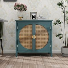 a blue cabinet with wicker doors in front of a wallpapered wall and potted plants