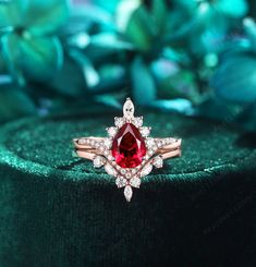 a ring with a large red stone surrounded by small white diamonds on top of a green velvet cushion