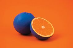 two oranges sitting next to each other on an orange background with one cut in half