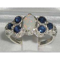 This Beautiful and Unusual Victorian Style Ring is made completely from Solid Sterling Silver and was Hallmarked in London, England.It has been hand set with a beautiful selection of Opal & Sapphires. These are genuine Opal Gemstones and a Natural Sapphires. These Colorful Vibrant Opal stand out wonderfully set against the polished Silver and contrast with the Vibrancy of the Sapphires providing such an Elegant overall appearance.The ring also boasts a well crafted Art Nouveau Style carving Opal And Sapphire Ring, Victorian Style Rings, Art Nouveau Ring, Carved Ring, Precious Opal, Daisy Ring, Sapphire Engagement Ring Blue, Pave Ring, Stone Engagement Rings