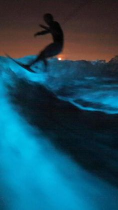 a man riding a wave on top of a surfboard in the ocean at night