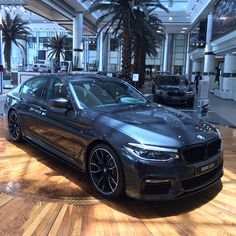 a car is parked in a showroom with palm trees and other cars behind it