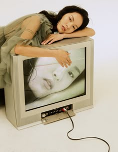 a woman laying on top of a tv with her head resting on the television screen