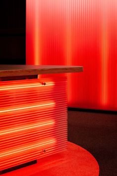 a red wall behind a counter with a wooden table in front of it and an orange light shining on the floor