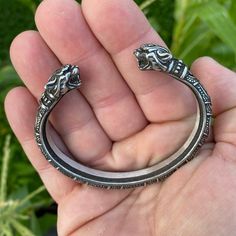 a hand holding a silver ring with two elephants on it's side, in front of some plants