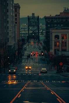 cars are driving down the street at night in an urban area with tall buildings and traffic lights