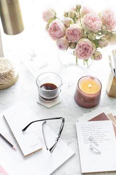 a table topped with pink flowers next to a vase filled with roses and writing utensils