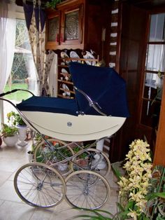 a white and blue baby carriage sitting in a living room next to a flower pot