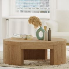 a round coffee table with some books and vases on it in front of a window