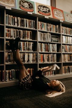 a woman laying on the floor in front of a bookshelf reading a book