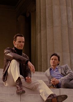 two men sitting on the steps of a building, one with his foot up to another man's knee