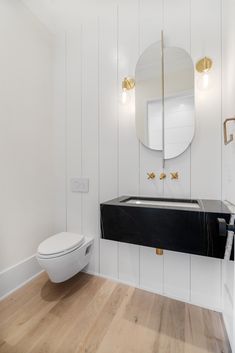 a white bathroom with black counter top and gold accents on the mirror over the toilet