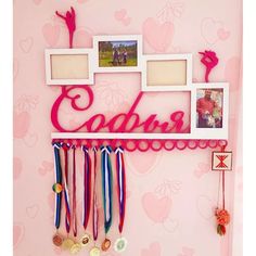 there is a pink wall with pictures and medals hanging from it's hooks on the wall