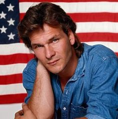 a man sitting in front of an american flag with his hand on his chin and looking at the camera