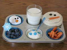 a muffin tin filled with cupcakes, carrots and blueberries next to a glass of milk