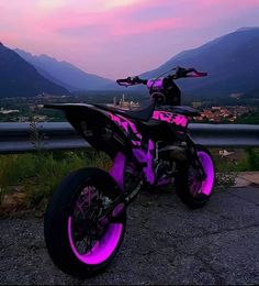 a purple and black dirt bike parked on the side of a road at dusk with mountains in the background