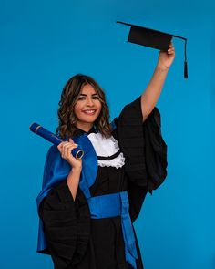 a woman in a graduation gown holding her diploma and posing for the camera on a blue background