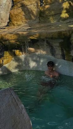 a man is in the water with a surfboard near some rocks and a waterfall