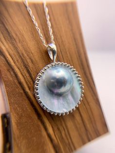 This exquisite necklace showcases a lustrous Mabe pearl of remarkable proportions, measuring a stunning 20 mm in width and rising majestically 8mm above the sterling silver setting. The focal point of this pendant is the remarkable Mabe pearl, boasting a smooth, round surface that radiates a captivating luster, capturing the essence of natural beauty. Nestled within a meticulously crafted regency-inspired bezel setting, the pearl is showcased in all its glory, echoing the opulence of 19th-centur White Gold Mother Of Pearl Pendant Necklace, Elegant Tahitian Pearl Drop Necklace, Pearl Drop Medallion Jewelry Gift, Silver Medallion Jewelry With Pearl Chain, Exquisite Silver Necklace With Pearl Drop, Luxury Silver Pearl Pendant Jewelry, Silver Jewelry With Round Pearl Pendant, Elegant Large Pendant Mother Of Pearl Jewelry, Classic Round Tahitian Pearl Necklaces