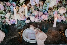 the table is set with pink and blue flowers, candles, and place settings for dinner