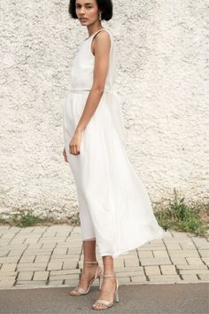 a woman in a white dress is standing on the sidewalk