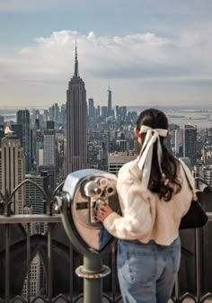 a woman looking at the empire building through a telescope on top of a skyscraper in new york city