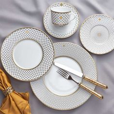 white and gold dinnerware set on a bed with silver napkins, fork and knife