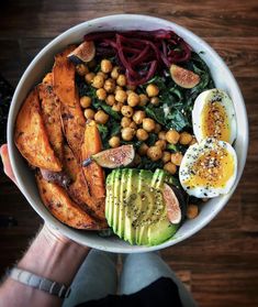 a person holding up a bowl filled with vegetables, eggs and other foods on top of it