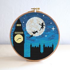 a cross stitch picture of a clock tower with a full moon in the background