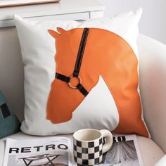 an orange horse pillow sitting on top of a white chair next to a coffee cup