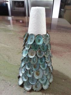 a vase made out of seashells sitting on top of a kitchen counter next to a roll of toilet paper