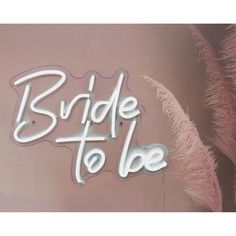 the bride to be neon sign is hanging on the wall next to some pink feathers