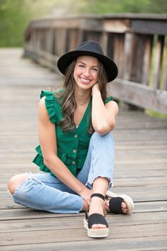 a woman sitting on the ground wearing a black hat and green shirt with her legs crossed