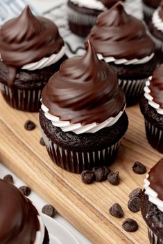 chocolate cupcakes with white frosting and chocolate chips on a cutting board next to plates